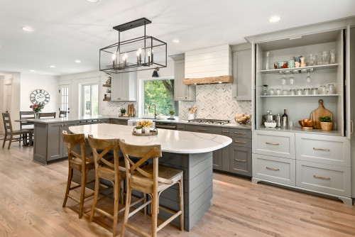 Modern farmhouse kitchen with two-tone gray shaker RTA cabinets, large shiplap island with rounded quartz top, brass hardware, and chevron backsplash.