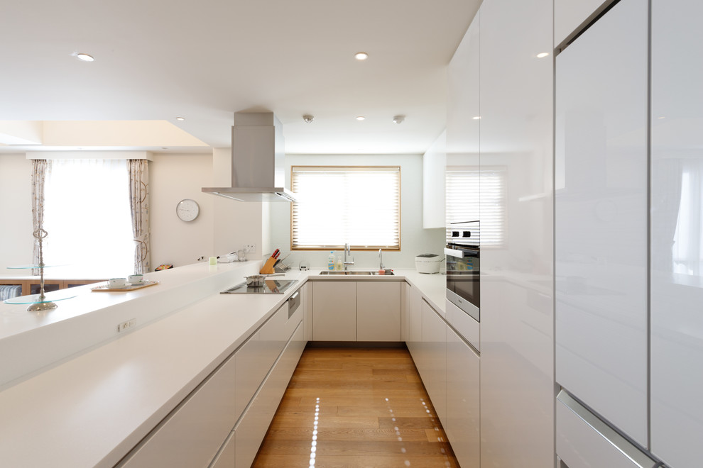 Inspiration for a large modern u-shaped open plan kitchen in Tokyo with an undermount sink, flat-panel cabinets, white cabinets, solid surface benchtops, white splashback, glass sheet splashback, stainless steel appliances, plywood floors, with island and brown floor.