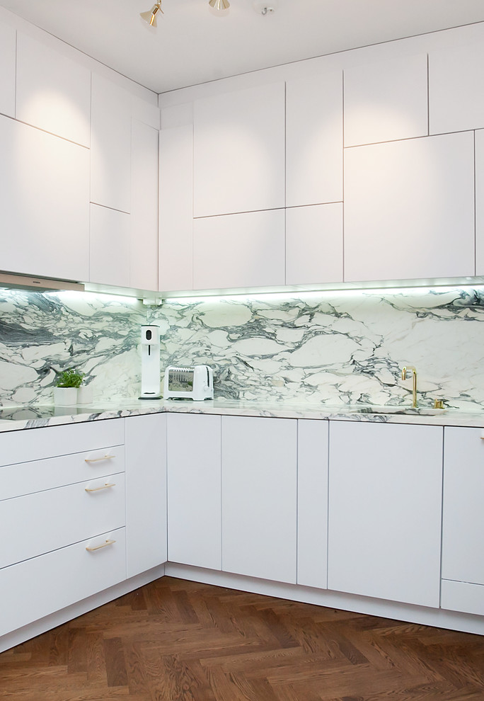 Photo of a mid-sized contemporary l-shaped kitchen in Stockholm with a drop-in sink, flat-panel cabinets, white cabinets, marble benchtops, white appliances, medium hardwood floors and no island.