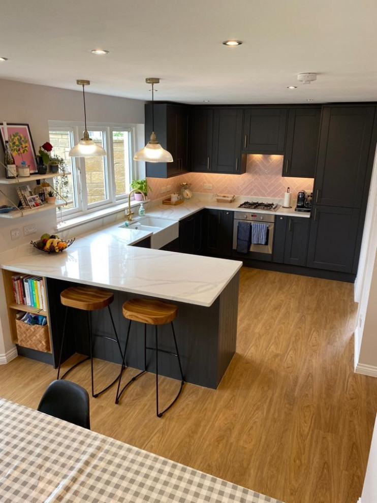 Inspiration for a mid-sized contemporary l-shaped eat-in kitchen in Edinburgh with a double-bowl sink, shaker cabinets, black cabinets, quartzite benchtops, pink splashback, ceramic splashback, stainless steel appliances, light hardwood floors and white benchtop.