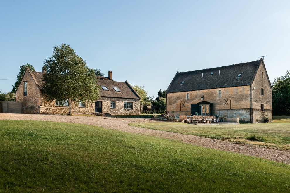 Photo of an expansive and beige rural brick detached house in Gloucestershire with three floors, a pitched roof and a black roof.