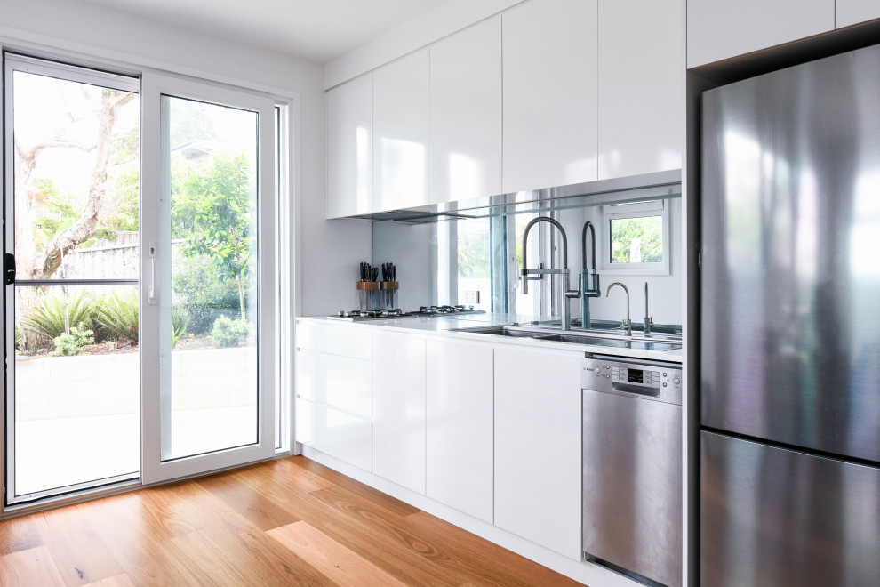 Idéer för att renovera ett litet funkis vit linjärt vitt kök med öppen planlösning, med en undermonterad diskho, vita skåp, bänkskiva i kvarts, flerfärgad stänkskydd, spegel som stänkskydd, integrerade vitvaror, en köksö och brunt golv