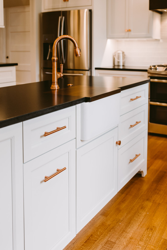 Example of a mid-sized transitional u-shaped medium tone wood floor and brown floor eat-in kitchen design in Baltimore with a farmhouse sink, shaker cabinets, white cabinets, quartz countertops, blue backsplash, glass tile backsplash, stainless steel appliances, an island and black countertops