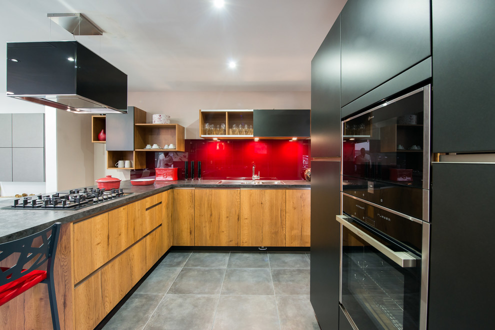 Design ideas for a contemporary l-shaped open plan kitchen in London with a double-bowl sink, flat-panel cabinets, black cabinets, laminate benchtops, red splashback, black appliances and glass sheet splashback.