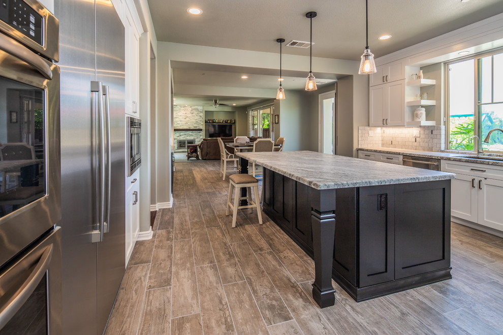 This is an example of a mid-sized transitional u-shaped open plan kitchen in San Diego with an undermount sink, recessed-panel cabinets, white cabinets, quartz benchtops, grey splashback, porcelain splashback, stainless steel appliances, porcelain floors, with island, grey floor and grey benchtop.