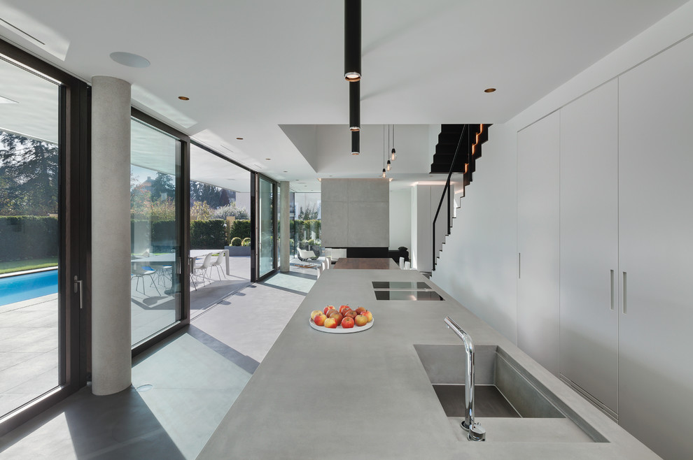 Expansive contemporary galley open plan kitchen in Munich with an integrated sink, flat-panel cabinets, grey cabinets, concrete benchtops, concrete floors, multiple islands and grey floor.