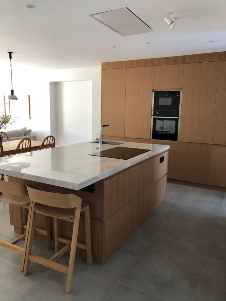 Large scandinavian single-wall open plan kitchen in Other with an undermount sink, flat-panel cabinets, medium wood cabinets, granite benchtops, panelled appliances, concrete floors, with island, grey floor and beige benchtop.