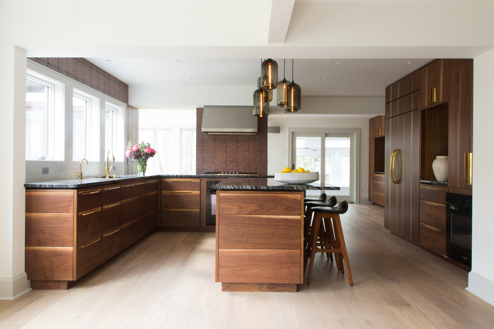 Design ideas for an eclectic eat-in kitchen in New York with marble benchtops, with island, flat-panel cabinets, medium wood cabinets, black appliances, an undermount sink and light hardwood floors.