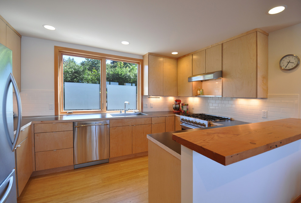 Photo of a small contemporary u-shaped open plan kitchen in Seattle with a drop-in sink, flat-panel cabinets, light wood cabinets, wood benchtops, white splashback, subway tile splashback, stainless steel appliances and bamboo floors.
