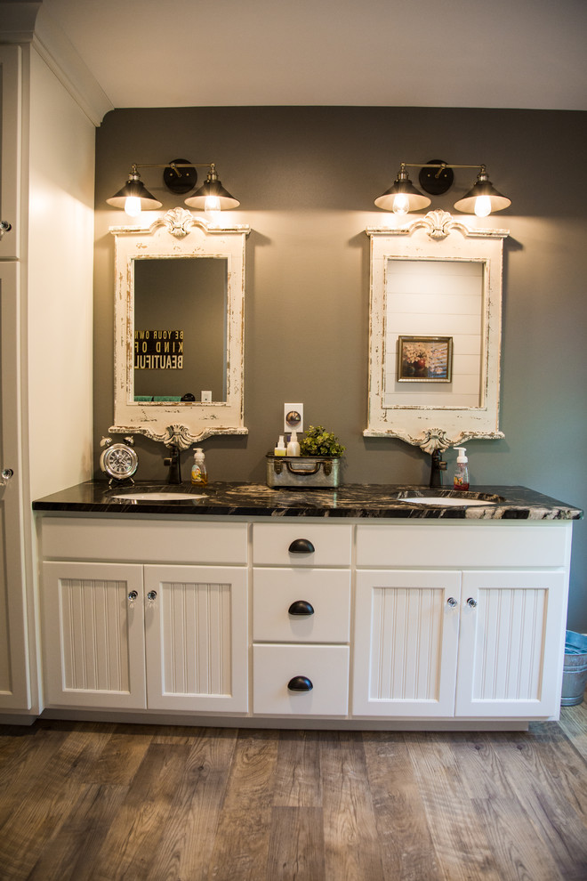 This is an example of a mid-sized country kids bathroom in Other with beaded inset cabinets, white cabinets, an alcove tub, a shower/bathtub combo, a one-piece toilet, grey walls, vinyl floors, an undermount sink, granite benchtops, brown floor, a shower curtain and black benchtops.