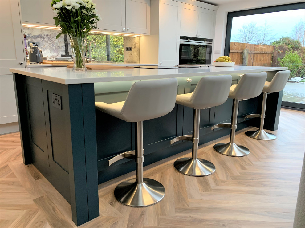 Inspiration for a large traditional single-wall open plan kitchen in Other with a single-bowl sink, shaker cabinets, medium wood cabinets, quartzite benchtops, glass sheet splashback, black appliances, vinyl floors, with island and white benchtop.