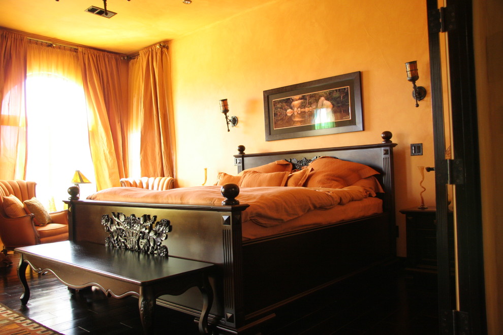 This is an example of a mid-sized mediterranean guest bedroom in Sacramento with orange walls and dark hardwood floors.
