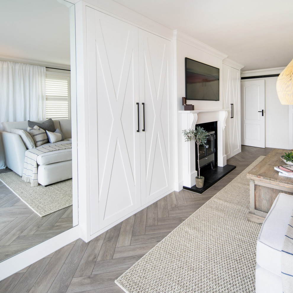 Foto på ett maritimt separat vardagsrum, med en hemmabar, vita väggar, laminatgolv, en öppen vedspis, en spiselkrans i trä, en väggmonterad TV och brunt golv