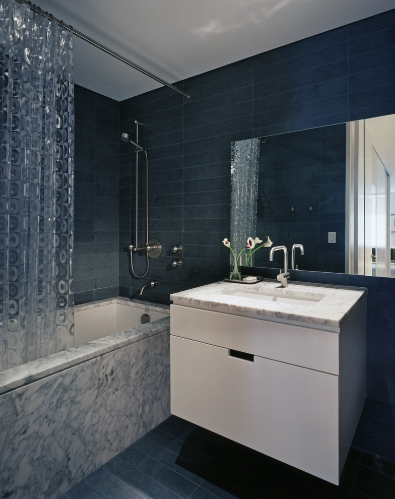 Photo of a contemporary bathroom in New York with an undermount sink, flat-panel cabinets, white cabinets, an alcove tub, a shower/bathtub combo, gray tile and a shower curtain.
