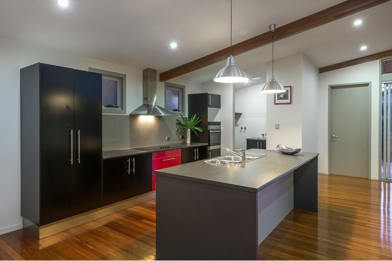 Mid-sized contemporary single-wall eat-in kitchen in Brisbane with recessed-panel cabinets, black cabinets, laminate benchtops, metallic splashback, glass sheet splashback, stainless steel appliances, medium hardwood floors and with island.