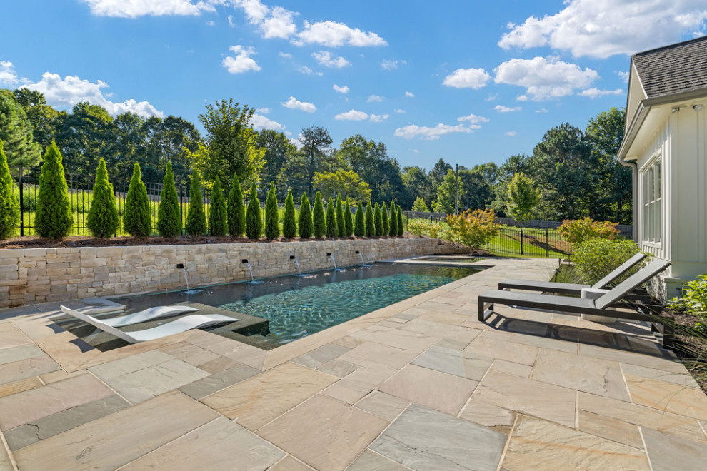Foto de piscina actual grande rectangular en patio trasero con privacidad y adoquines de piedra natural