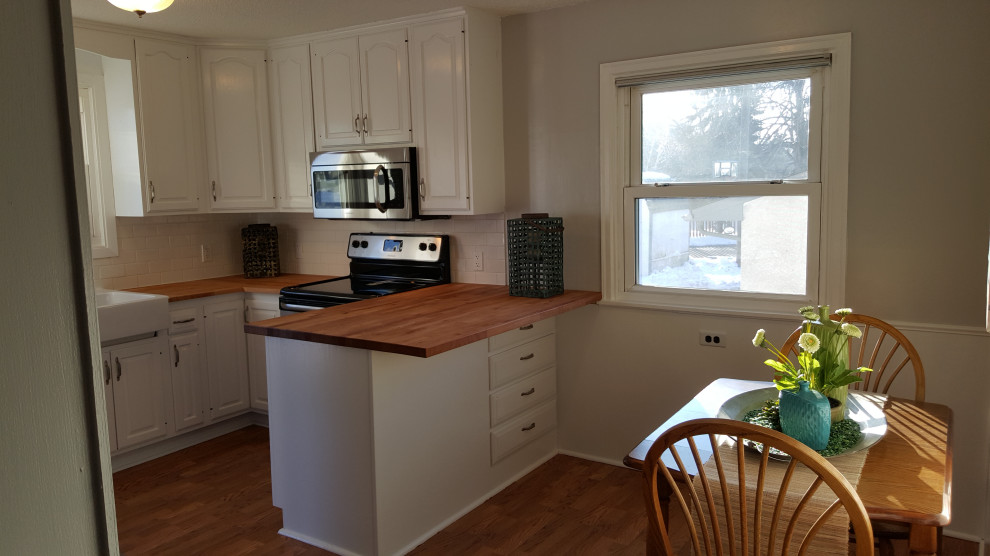 ミネアポリスにある高級なシャビーシック調のおしゃれなキッチン (白いキャビネット、木材カウンター、シルバーの調理設備、クッションフロア) の写真