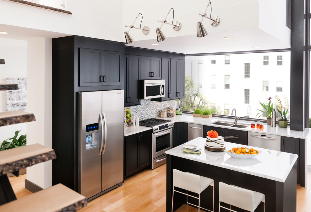 Photo of a mid-sized modern l-shaped eat-in kitchen in Philadelphia with a double-bowl sink, shaker cabinets, black cabinets, quartzite benchtops, grey splashback, mosaic tile splashback, stainless steel appliances, light hardwood floors, with island and beige floor.