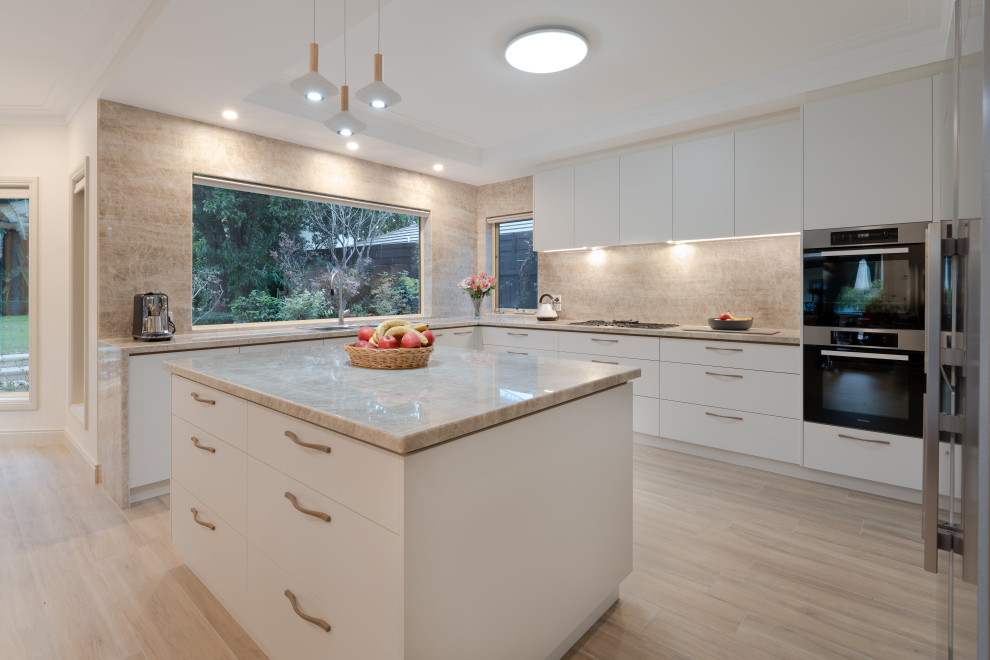 This is an example of a large modern u-shaped kitchen in Melbourne with a double-bowl sink, flat-panel cabinets, white cabinets, granite benchtops, brown splashback, granite splashback, stainless steel appliances, light hardwood floors, with island, beige floor and brown benchtop.