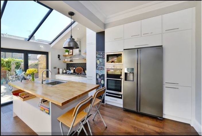 This is an example of a large contemporary galley eat-in kitchen in London with a drop-in sink, white cabinets, wood benchtops, grey splashback, ceramic splashback, stainless steel appliances, dark hardwood floors and with island.