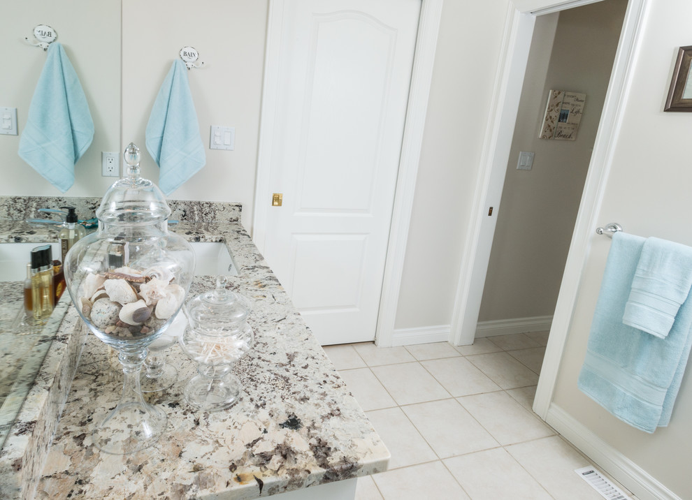 Photo of a small transitional master bathroom in Edmonton with shaker cabinets, white cabinets, a corner tub, a corner shower, a one-piece toilet, multi-coloured tile, pebble tile, beige walls, porcelain floors, a drop-in sink and granite benchtops.