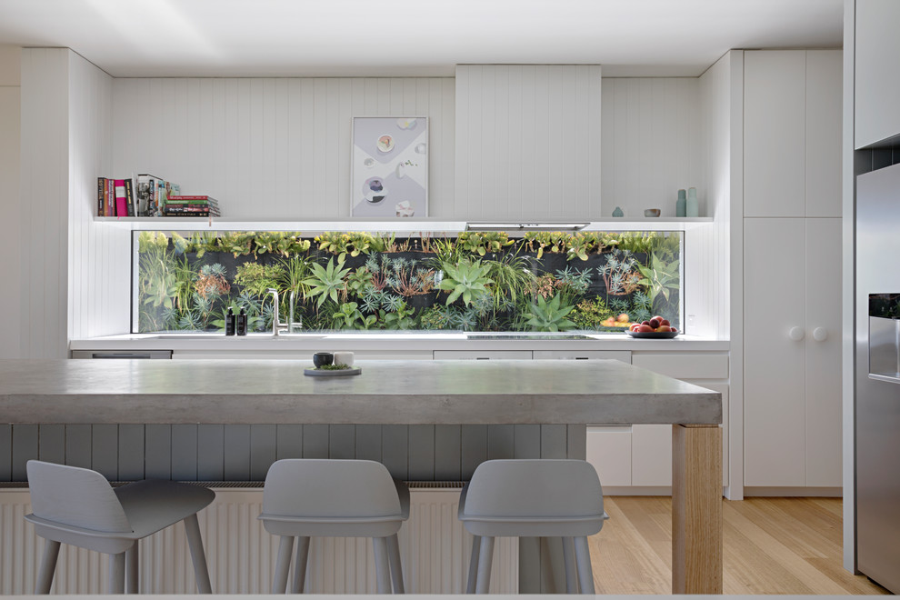 Inspiration for a modern open plan kitchen in Melbourne with flat-panel cabinets, white cabinets, concrete benchtops, window splashback, stainless steel appliances, light hardwood floors, with island and beige floor.