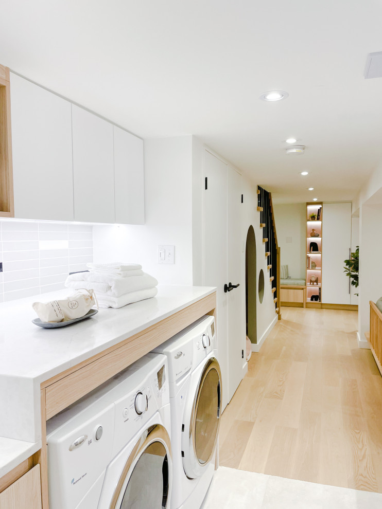 This is an example of a large scandinavian galley laundry room in Toronto with an utility sink, flat-panel cabinets, light wood cabinets, quartz benchtops, multi-coloured splashback, porcelain splashback, white walls, ceramic floors, a side-by-side washer and dryer, grey floor and grey benchtop.