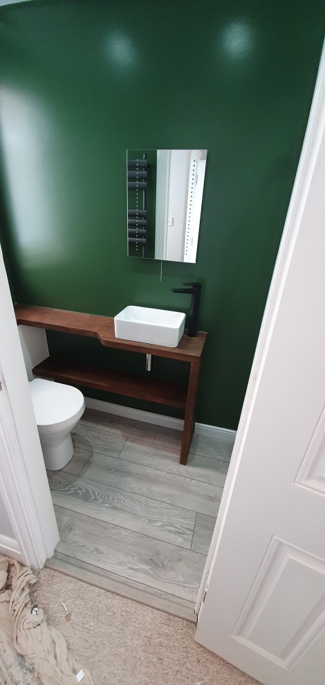 Inredning av ett modernt litet brun brunt badrum, med släta luckor, vita skåp, en öppen dusch, en toalettstol med hel cisternkåpa, gröna väggar, laminatgolv, ett avlångt handfat, träbänkskiva, grått golv och dusch med gångjärnsdörr