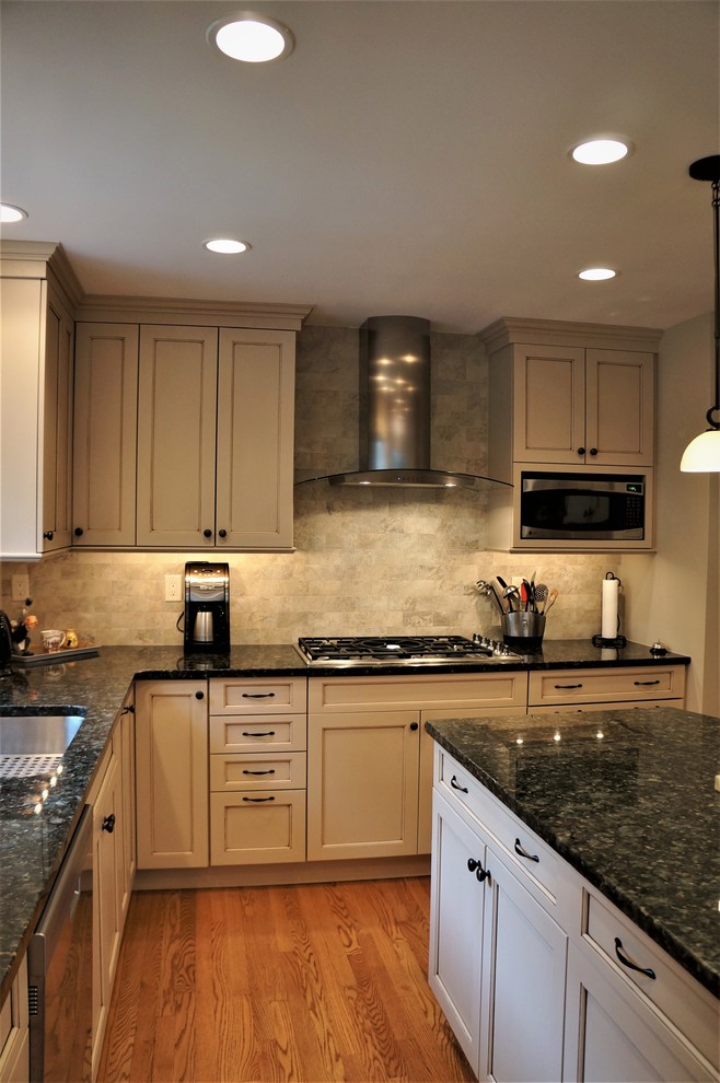 Inspiration for a mid-sized transitional l-shaped medium tone wood floor and brown floor open concept kitchen remodel in Boston with an undermount sink, recessed-panel cabinets, beige cabinets, granite countertops, beige backsplash, subway tile backsplash, stainless steel appliances, an island and black countertops