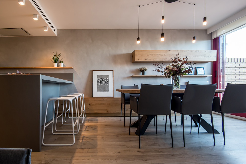 This is an example of a large contemporary open plan dining in Barcelona with grey walls, laminate floors, a two-sided fireplace, a metal fireplace surround and brown floor.
