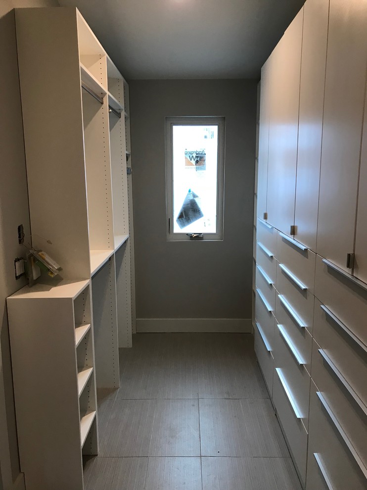 This is an example of a mid-sized traditional gender-neutral walk-in wardrobe in Other with flat-panel cabinets, white cabinets, ceramic floors and grey floor.