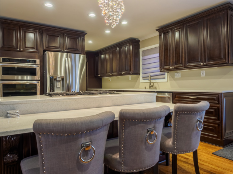Inspiration for a mid-sized transitional l-shaped open plan kitchen in Orlando with an undermount sink, raised-panel cabinets, dark wood cabinets, quartz benchtops, stainless steel appliances, medium hardwood floors, with island, brown floor and grey benchtop.