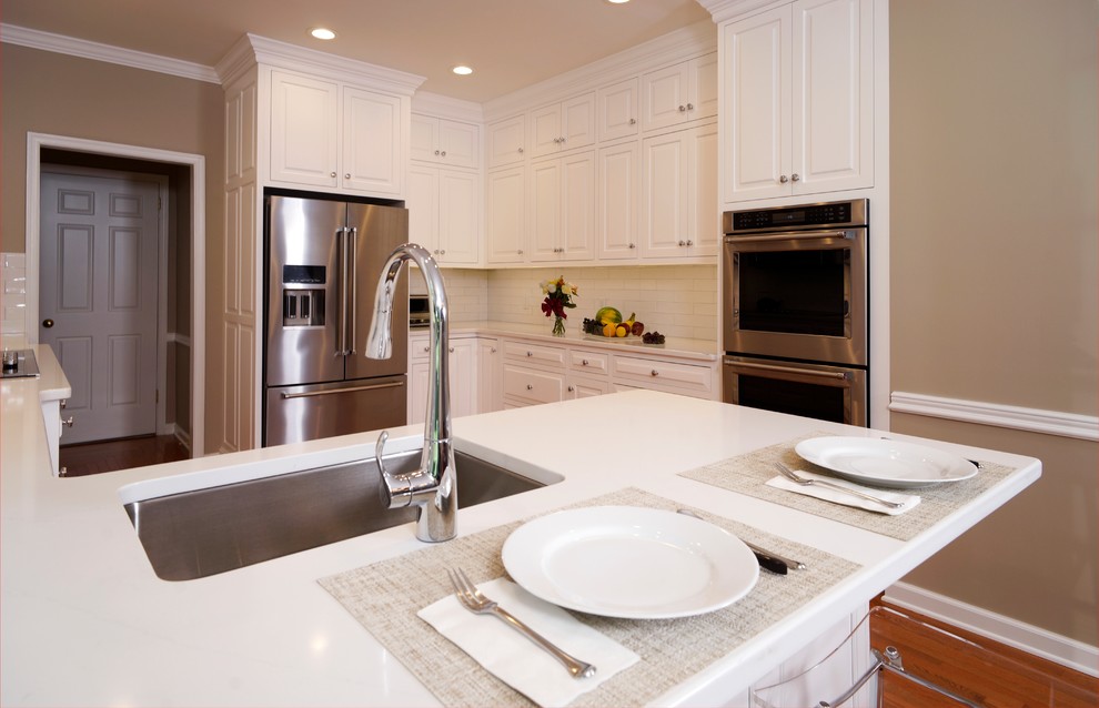 This is an example of a mid-sized traditional l-shaped eat-in kitchen in Philadelphia with an undermount sink, beaded inset cabinets, white cabinets, granite benchtops, white splashback, subway tile splashback, stainless steel appliances, medium hardwood floors, a peninsula, brown floor and white benchtop.
