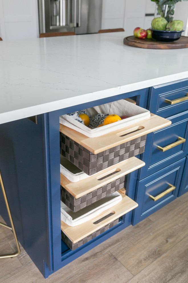 Large transitional l-shaped brown floor kitchen pantry photo in Baltimore with a drop-in sink, shaker cabinets, white cabinets, quartz countertops, white backsplash, ceramic backsplash, stainless steel appliances, an island and white countertops