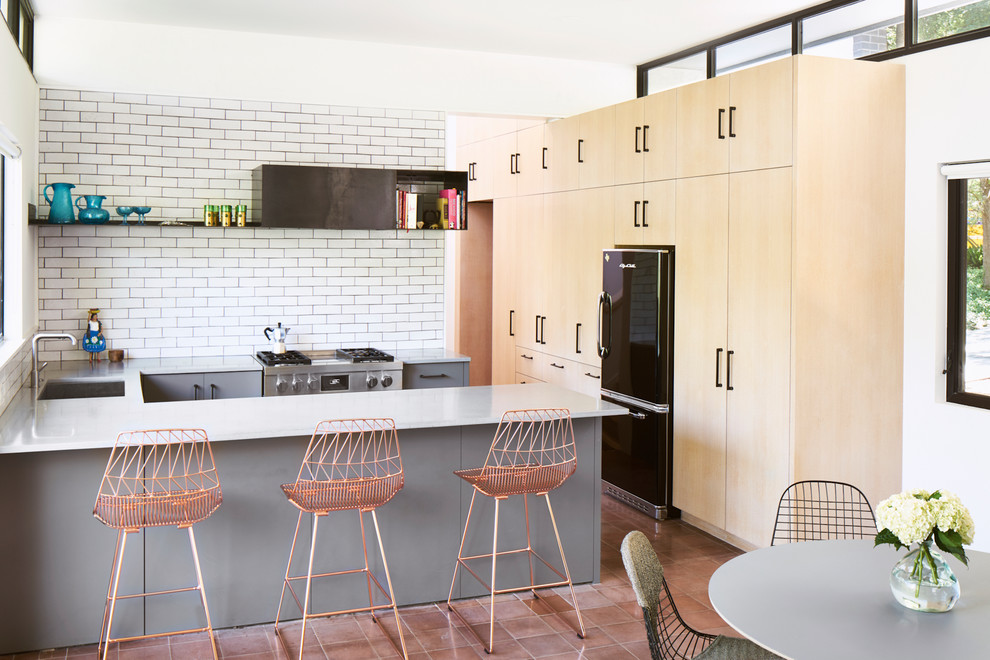 This is an example of a contemporary l-shaped open plan kitchen in Austin with an undermount sink, flat-panel cabinets, light wood cabinets, white splashback, subway tile splashback, stainless steel appliances, terra-cotta floors, a peninsula and pink floor.