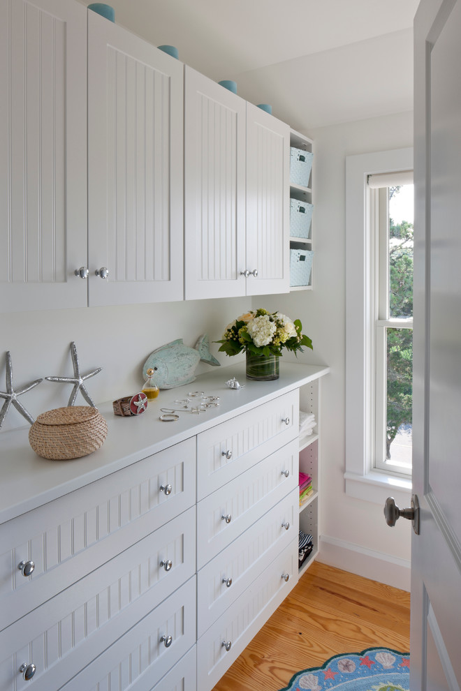 Inspiration for a mid-sized beach style single-wall dedicated laundry room in Boston with shaker cabinets, white cabinets, quartz benchtops, white walls, light hardwood floors and brown floor.