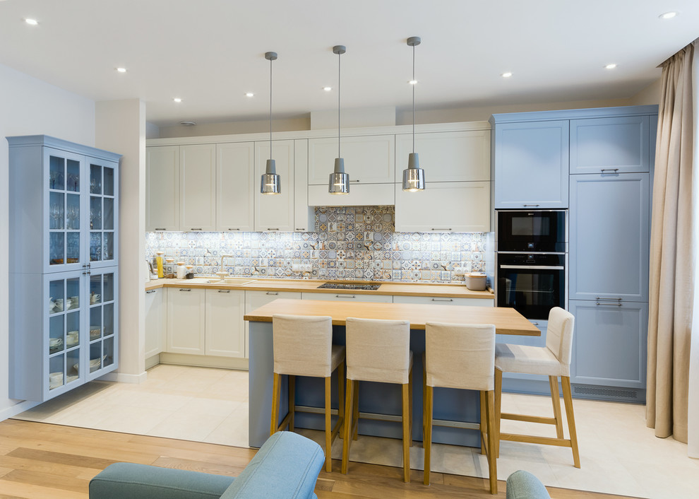 Inspiration for a transitional l-shaped open plan kitchen in Other with a drop-in sink, recessed-panel cabinets, blue cabinets, wood benchtops, multi-coloured splashback, with island, beige floor and brown benchtop.