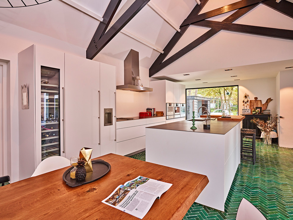 This is an example of an expansive contemporary galley eat-in kitchen in Other with an integrated sink, flat-panel cabinets, white cabinets, stainless steel benchtops, white splashback, stainless steel appliances, ceramic floors, with island and green floor.