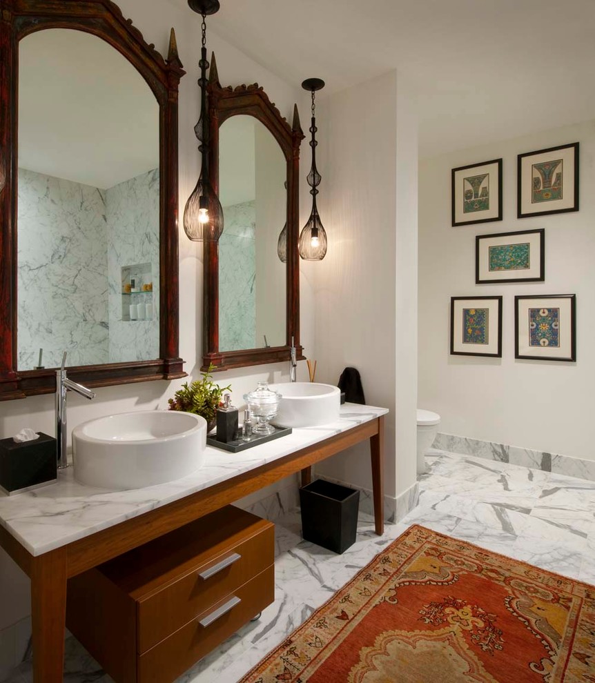 Large eclectic bathroom in Dallas with a vessel sink, medium wood cabinets, marble benchtops, a freestanding tub, a one-piece toilet, stone slab, white walls, marble floors and flat-panel cabinets.
