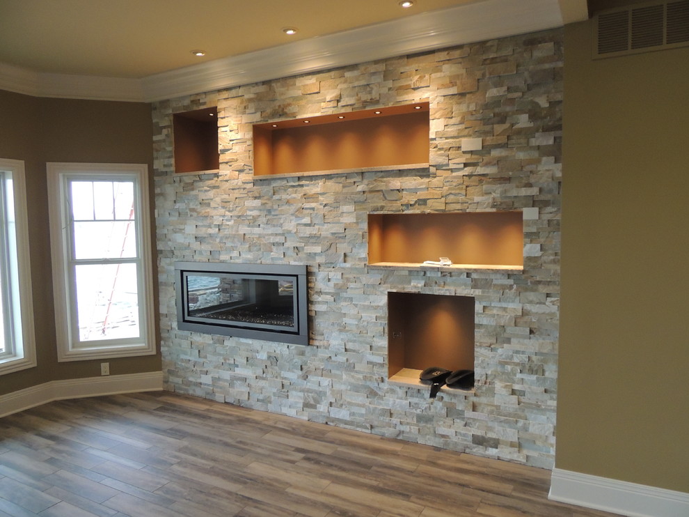 This is an example of an expansive arts and crafts walk-out basement in Other with beige walls, light hardwood floors, a ribbon fireplace, a stone fireplace surround and multi-coloured floor.