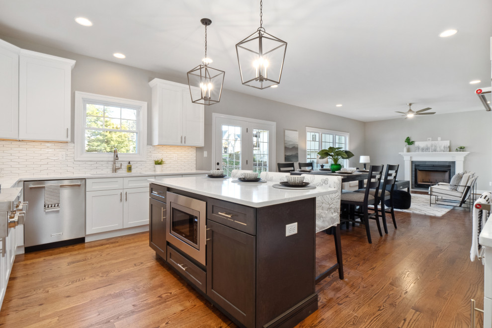 Inspiration for a transitional medium tone wood floor and brown floor kitchen remodel in St Louis with shaker cabinets, white cabinets, quartz countertops, white backsplash, ceramic backsplash, stainless steel appliances, an island and white countertops