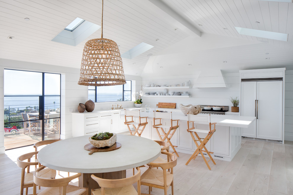 This is an example of a large country l-shaped open plan kitchen in Orange County with light hardwood floors, a farmhouse sink, shaker cabinets, white cabinets, marble benchtops, white splashback, shiplap splashback, stainless steel appliances, with island, beige floor and white benchtop.