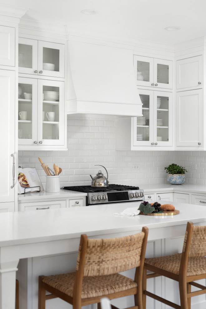Inspiration for a medium sized classic l-shaped kitchen/diner in Chicago with a belfast sink, beaded cabinets, white cabinets, engineered stone countertops, white splashback, ceramic splashback, integrated appliances, medium hardwood flooring, an island, brown floors and white worktops.