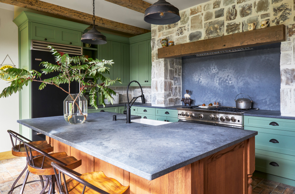 Bild på ett avskilt, mellanstort rustikt grå grått l-kök, med en rustik diskho, skåp i shakerstil, gröna skåp, bänkskiva i kvarts, grått stänkskydd, svarta vitvaror, tegelgolv, en köksö och brunt golv
