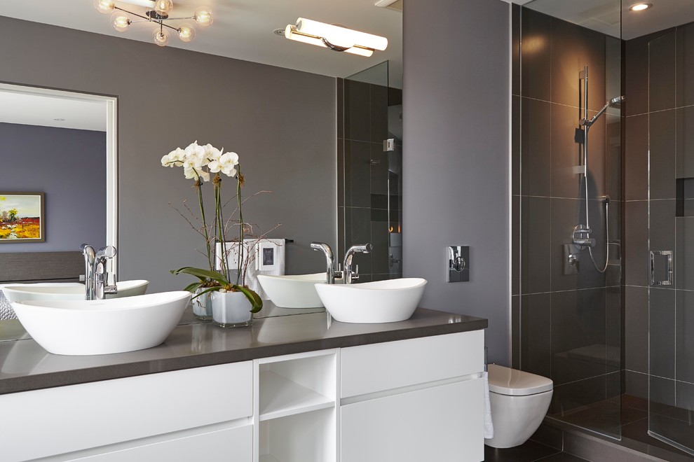 Large contemporary master bathroom in Toronto with flat-panel cabinets, white cabinets, a freestanding tub, an alcove shower, a wall-mount toilet, gray tile, porcelain tile, grey walls, porcelain floors, a vessel sink and engineered quartz benchtops.