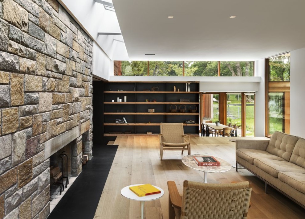 This is an example of a modern living room in New York with light hardwood floors, a standard fireplace and a stone fireplace surround.