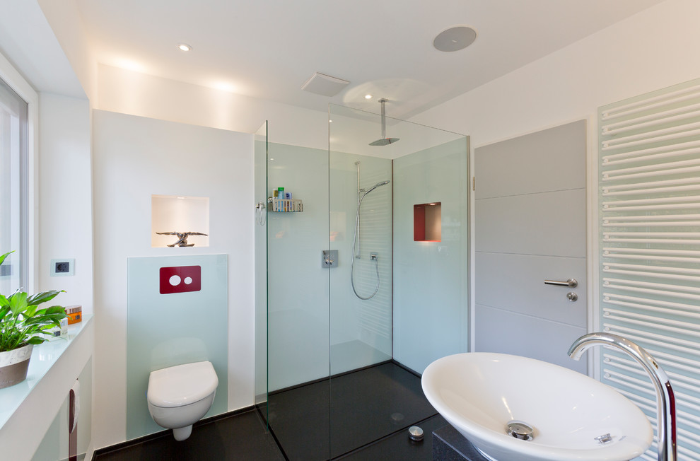 Photo of a mid-sized modern 3/4 bathroom in Hamburg with a curbless shower, a two-piece toilet, blue tile, glass sheet wall, white walls, a vessel sink, granite benchtops, black floor, an open shower and black benchtops.