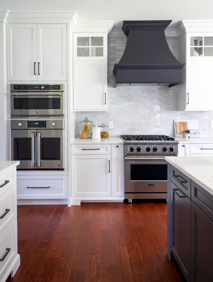 Transitional medium tone wood floor kitchen photo with an undermount sink, shaker cabinets, quartz countertops, gray backsplash, porcelain backsplash, stainless steel appliances, an island and white countertops