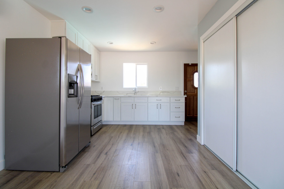 Mid-sized contemporary l-shaped eat-in kitchen in Los Angeles with a drop-in sink, white cabinets, granite benchtops, grey splashback, granite splashback, stainless steel appliances, laminate floors, brown floor, white benchtop and shaker cabinets.