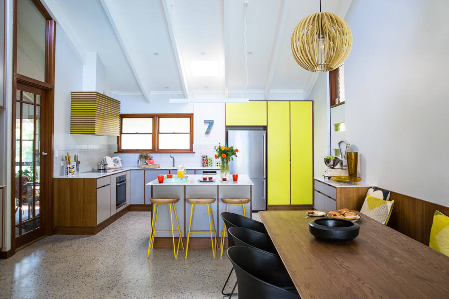 Expansive midcentury l-shaped open plan kitchen in Adelaide with an integrated sink, flat-panel cabinets, grey cabinets, solid surface benchtops, white splashback, porcelain splashback, stainless steel appliances, concrete floors and with island.